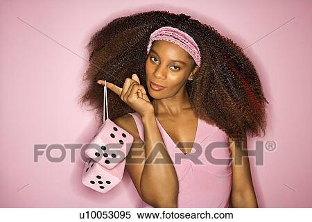 Stock Photography - Portrait of smiling young African-American adult woman on pink background holding fuzzy dice.. Fotosearch