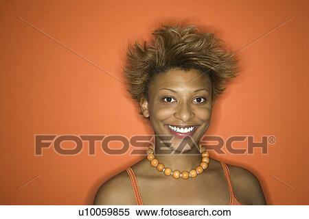 Stock Photography - Portrait of smiling young African-American adult woman on orange background.. Fotosearch