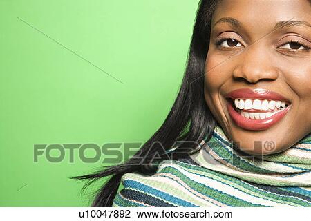 Stock Image - Smiling African-American mid-adult woman wearing green scarf on green background.. Fotosearch