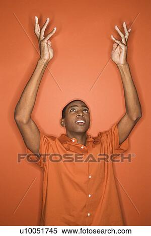 Stock Photography - Young African-American man throwing his arms up in the air wearing orange clothing on orange background.. Fotosearch