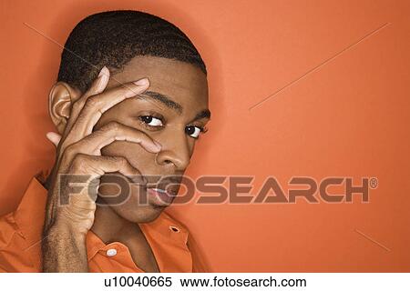 Stock Photography - Young African-American man with hand on his face on orange background.. Fotosearch