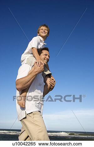 Stock Photography - Caucasian father with pre-teen on shoulders on beach.. Fotosearch