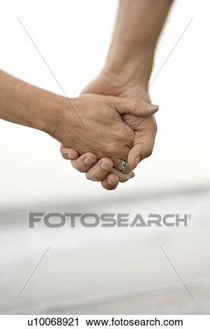 Stock Image - Caucasian man and woman holding hands on beach.. Fotosearch