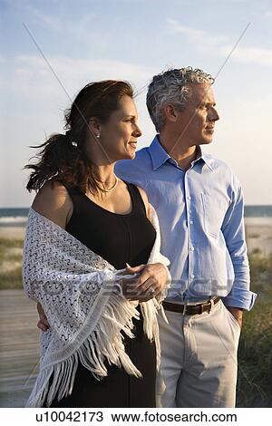 Stock Image - Caucasian mid-adult coulpe looking off to side at beach.. Fotosearch