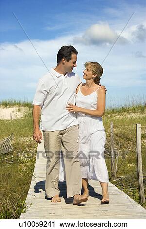Caucasian mid-adult couple holding each other walking down beach access path. View Large Photo Image Stock Image - Caucasian mid-adult couple holding each other walking down beach access path.. Fotosearch