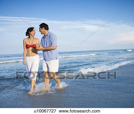 Caucasian mid-adult couple holding hands wading in ocean. View Large Photo Image Stock Photo - Caucasian mid-adult couple holding hands wading in ocean.. Fotosearch