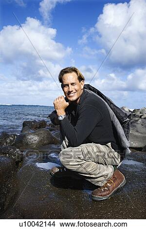 Caucasian mid-adult man kneeling on rocky coast looking at viewer smiling in Maui, Hawaii. View Large Photo Image Picture - Caucasian mid-adult man kneeling on rocky coast looking at viewer smiling in Maui, Hawaii.. Fotosearch