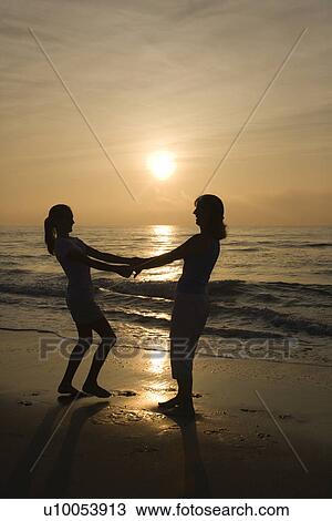 Caucasian mid-adult mother and teenage daughter holding hands spinngin on beach at sunset. View Large Photo Image Stock Image - Caucasian mid-adult mother and teenage daughter holding hands spinngin on beach at sunset.. Fotosearch