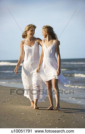 Stock Image - Caucasian mother and pre-teen girl walking on beach holding hands.. Fotosearch