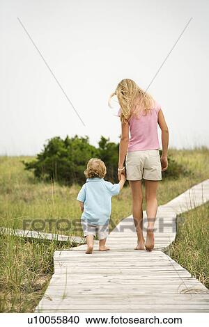 Caucasian pre-teen girl walking on beach access walkway and holding hands with Caucasian male toddler. View Large Photo Image Stock Image - Caucasian pre-teen girl walking on beach access walkway and holding hands with Caucasian male toddler.. Fotosearch