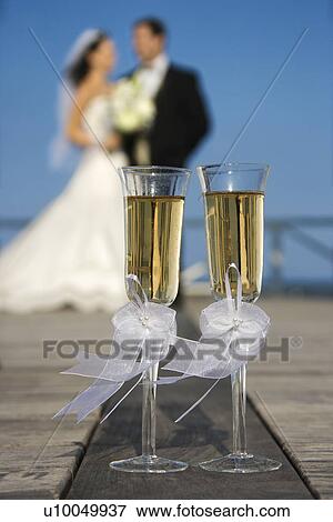 Pair of flute glasses of champagne with Caucasian bride and groom blurred in background. View Large Photo Image Stock Photo - Pair of flute glasses of champagne with Caucasian bride and groom blurred in background.. Fotosearch