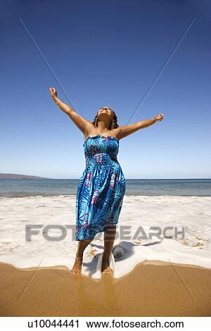 Stock Image - Yound-adult Black woman standing in shore with arms stretched.. Fotosearch