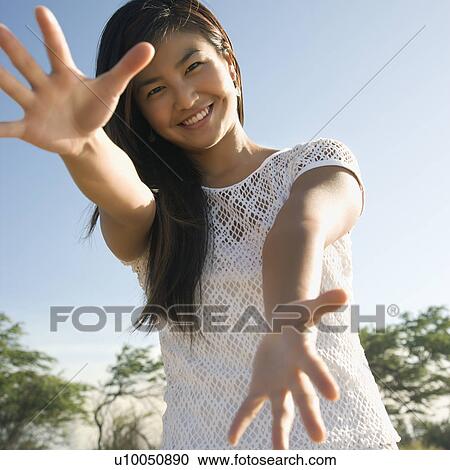 Stock Image - Young adult Asian female with arms and hands stretched out toward viewer.. Fotosearch