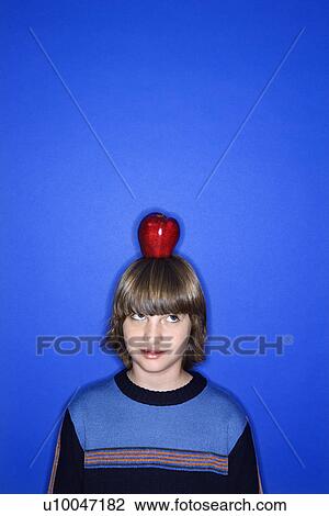 Head and shoulder portrait of Caucasian boy with apple on his head standing against blue background. View Large Photo Image Stock Image - Head and shoulder portrait of Caucasian boy with apple on his head standing against blue background.. Fotosearch