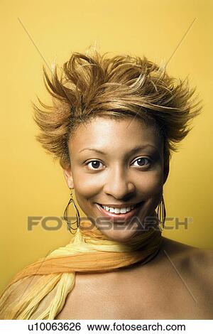 Stock Photograph - Head and shoulder portrait of smiling young African-American adult woman on yellow background.. Fotosearch