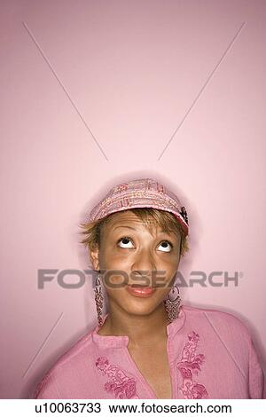 Stock Image - Head and shoulder portrait of young African-American adult woman on pink background looking up with eyes.. Fotosearch