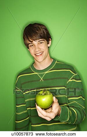 Stock Image - Portait of Caucasian teen boy holding apple.. Fotosearch