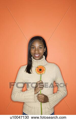 Portrait of African-American teen girl holding single Gerbera Daisy standing against orange background. View Large Photo Image Stock Image - Portrait of African-American teen girl holding single Gerbera Daisy standing against orange background.. Fotosearch
