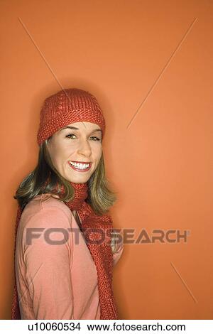 Portrait of smiling young adult Caucasian woman on orange background wearing winter hat and scarf. View Large Photo Image Picture - Portrait of smiling young adult Caucasian woman on orange background wearing winter hat and scarf.. Fotosearch