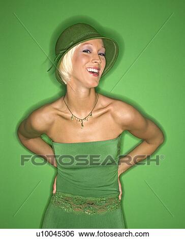 Stock Photograph - Portrait of smiling young adult Caucasian blond woman on green background wearing hat and sundress.. Fotosearch