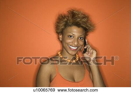 Portrait of smiling young African American adult woman on orange background talking on cellphone. View Large Photo Image Stock Photo - Portrait of smiling young African American adult woman on orange background talking on cellphone.. Fotosearch