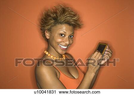 Stock Image - Portrait of smiling young African-American adult woman on orange background using her palmtop computer.. Fotosearch