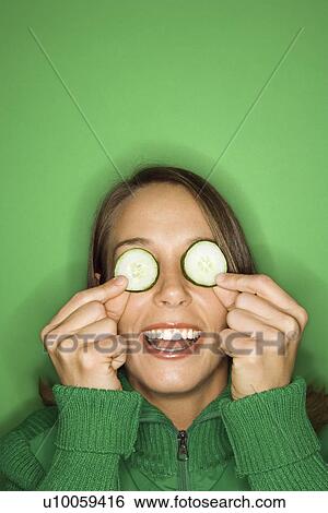 Portrait of young adult Caucasian woman on green background holding cucumber slices over her eyes. View Large Photo Image Stock Photograph - Portrait of young adult Caucasian woman on green background holding cucumber slices over her eyes.. Fotosearch