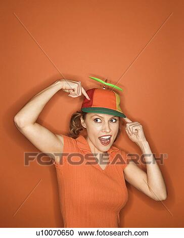 Smiling Caucasian mid-adult woman pointing and wearing propeller cap on orange background. View Large Photo Image Stock Image - Smiling Caucasian mid-adult woman pointing and wearing propeller cap on orange background.. Fotosearch
