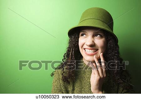Stock Image - Smiling young Caucasian woman on green background wearing green clothing and hat.. Fotosearch