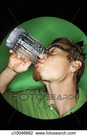 Stock Image - Vignette of adult Caucasian man on green background wearing green hat and drinking beer.. Fotosearch