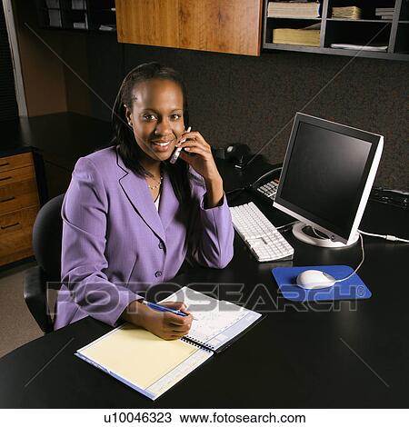 African-American young adult business woman talking on cell phone and writing in planner in office smiling and looking at viewer. View Large Photo Image Stock Image - African-American young adult business woman talking on cell phone and writing in planner in office smiling and looking at viewer.. Fotosearch