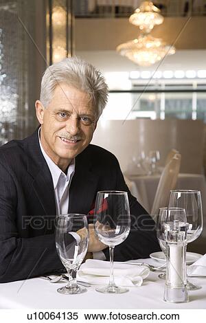 Caucasian mature adult male sitting at restaurant table looking at viewer smiling. View Large Photo Image Stock Photography - Caucasian mature adult male sitting at restaurant table looking at viewer smiling.. Fotosearch
