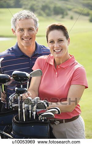 Stock Photo - Caucasion mid-adult man and woman with golf clubs smiling and looking at viewer.. Fotosearch