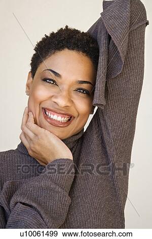 Stock Photo - Close up of African- American woman with head on hand looking at viewer smiling.. Fotosearch