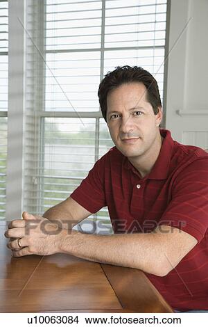 Picture - Portrait of Caucasian mid-adult man sitting at table, looking at viewer, smiling.. Fotosearch