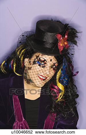 Stock Image - Portrait of Caucasian woman in unique makeup and clothing against purple background.. Fotosearch