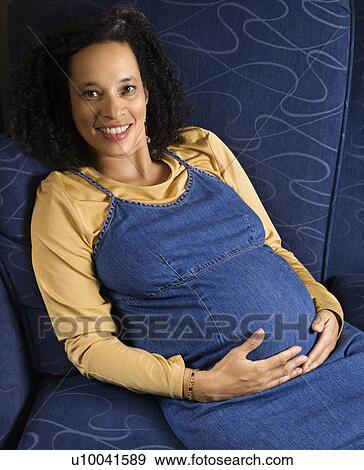 Portrait of young pregnant female with hands on stomach and looking at viewer. View Large Photo Image Stock Photo - Portrait of young pregnant female with hands on stomach and looking at viewer.. Fotosearch
