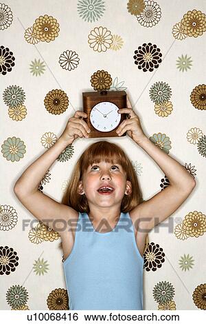 Stock Photograph - Caucasian female child holding clock over head.. Fotosearch