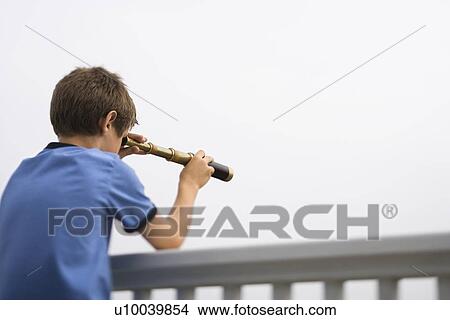 Picture - Caucasian pre-teen boy leaning on railing looking through telescope.. Fotosearch