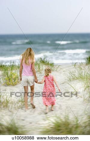 Stock Photo - Caucasian pre-teen girl holding hands with younger Caucasian girl walking toward beach.. Fotosearch