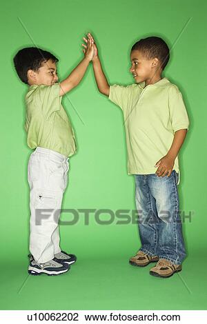 Stock Image - Hispanic and African American male child giving high five.. Fotosearch
