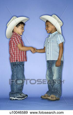 Stock Photo - Hispanic and African American male child in cowboy hats shaking hands.. Fotosearch