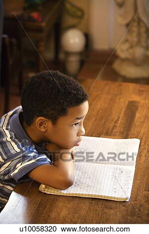 Stock Image - Portrait of young boy with head on arms with book in front.. Fotosearch