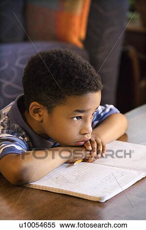Stock Photography - Portrait of young boy with head on arms with book in front.. Fotosearch