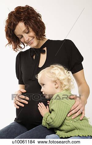 Picture - Young Caucasian female child with ear against her mother's pregnant belly.. Fotosearch