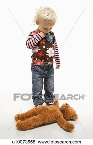 Stock Photo - Young Caucasian female toddler looking at her teddy bear on ground.. Fotosearch