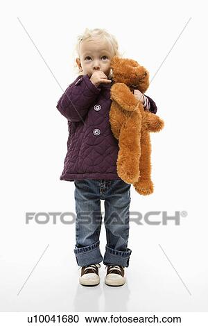 Stock Image - Young Caucasian female toddler sucking her thumb and holding her teddy bear.. Fotosearch