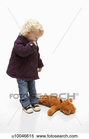 Stock Photography - Young Caucasian female toddler sucking her thumb and looking at her teddy bear on ground.. Fotosearch