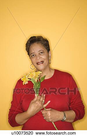 Stock Image - African American mature adult female holding flowers.. Fotosearch