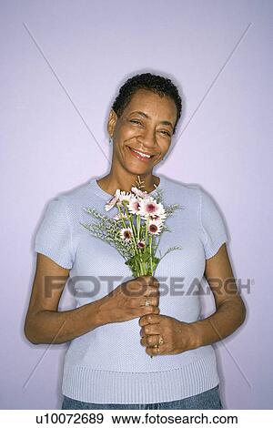 Stock Photo - African American mature adult female holding flowers.. Fotosearch